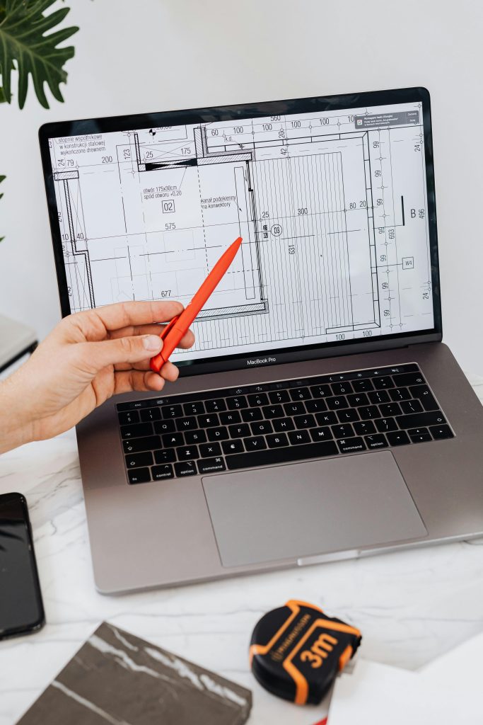 A hand using a red pen points at a floor plan displayed on a laptop, showcasing architectural design.