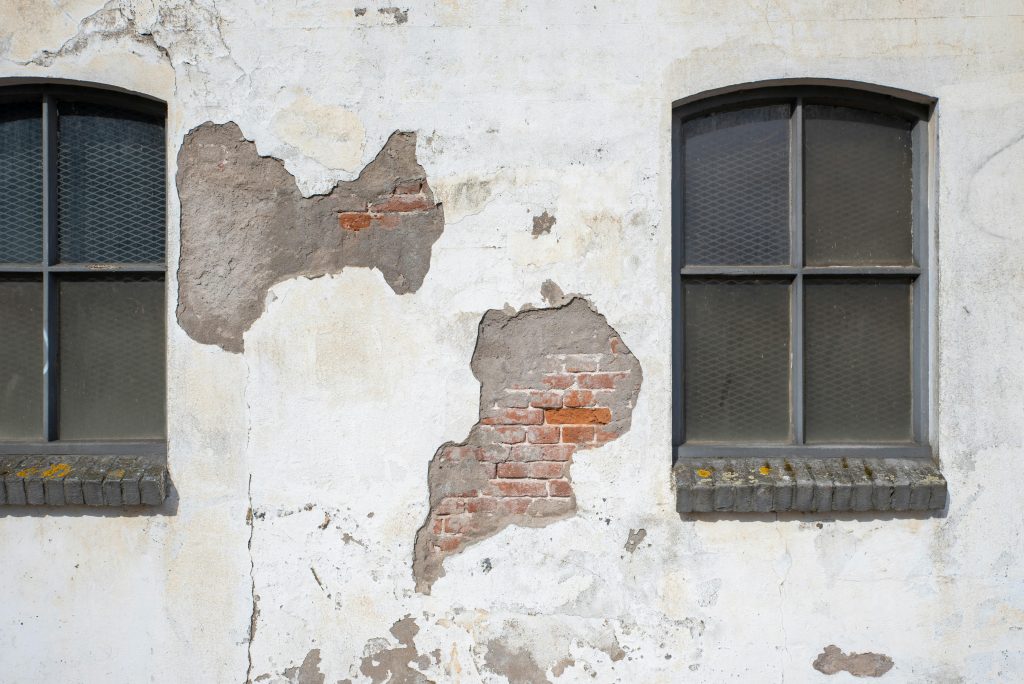 A rustic brick facade shows through worn plaster, flanking two vintage windows.